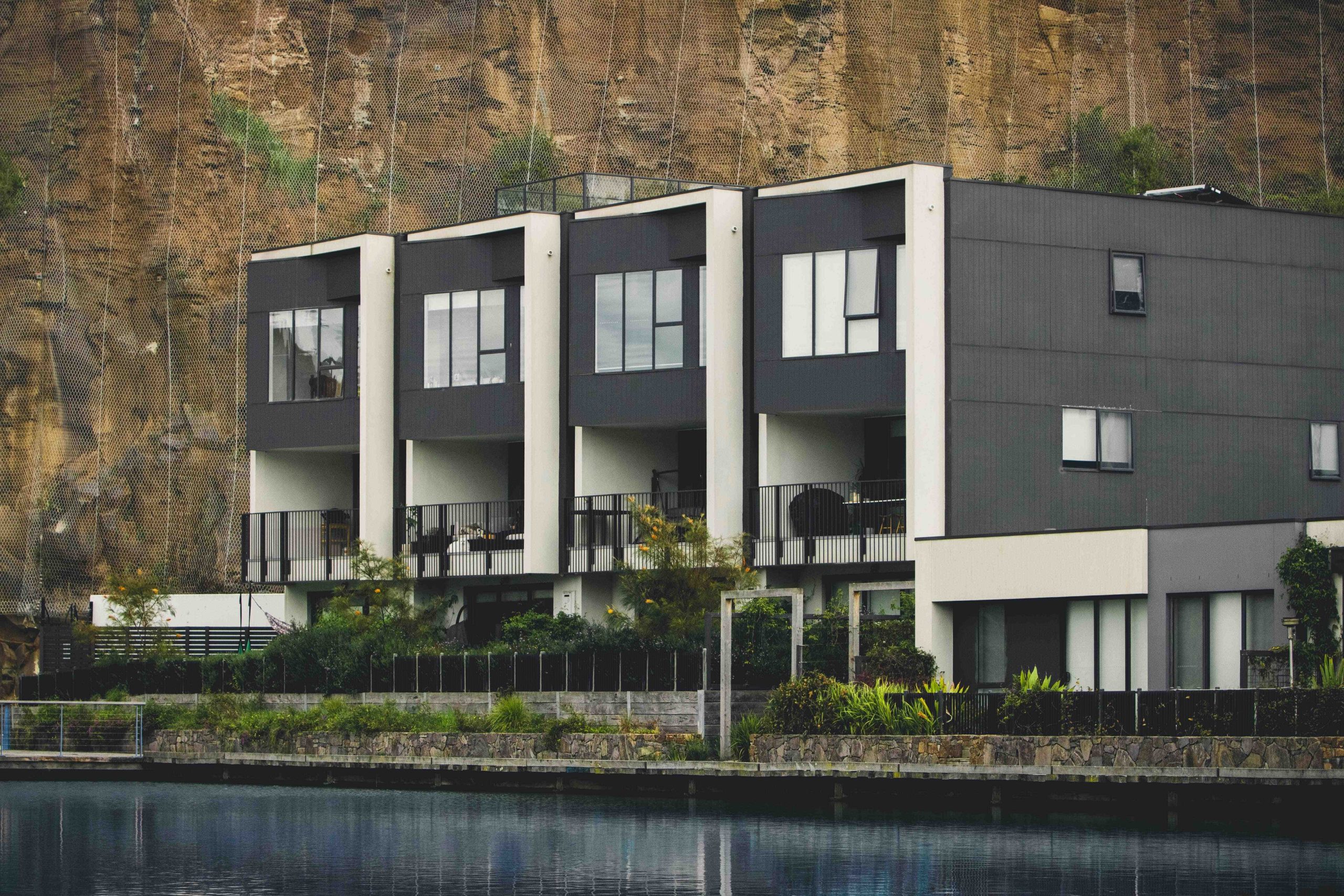 Modern waterfront condominium buildings with balconies below a steep rock cliff.