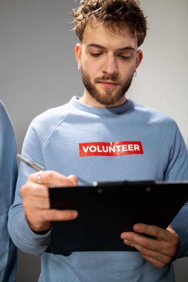 Volunteer in a blue sweatshirt writing on a clipboard, representing organized and manageable community participation.