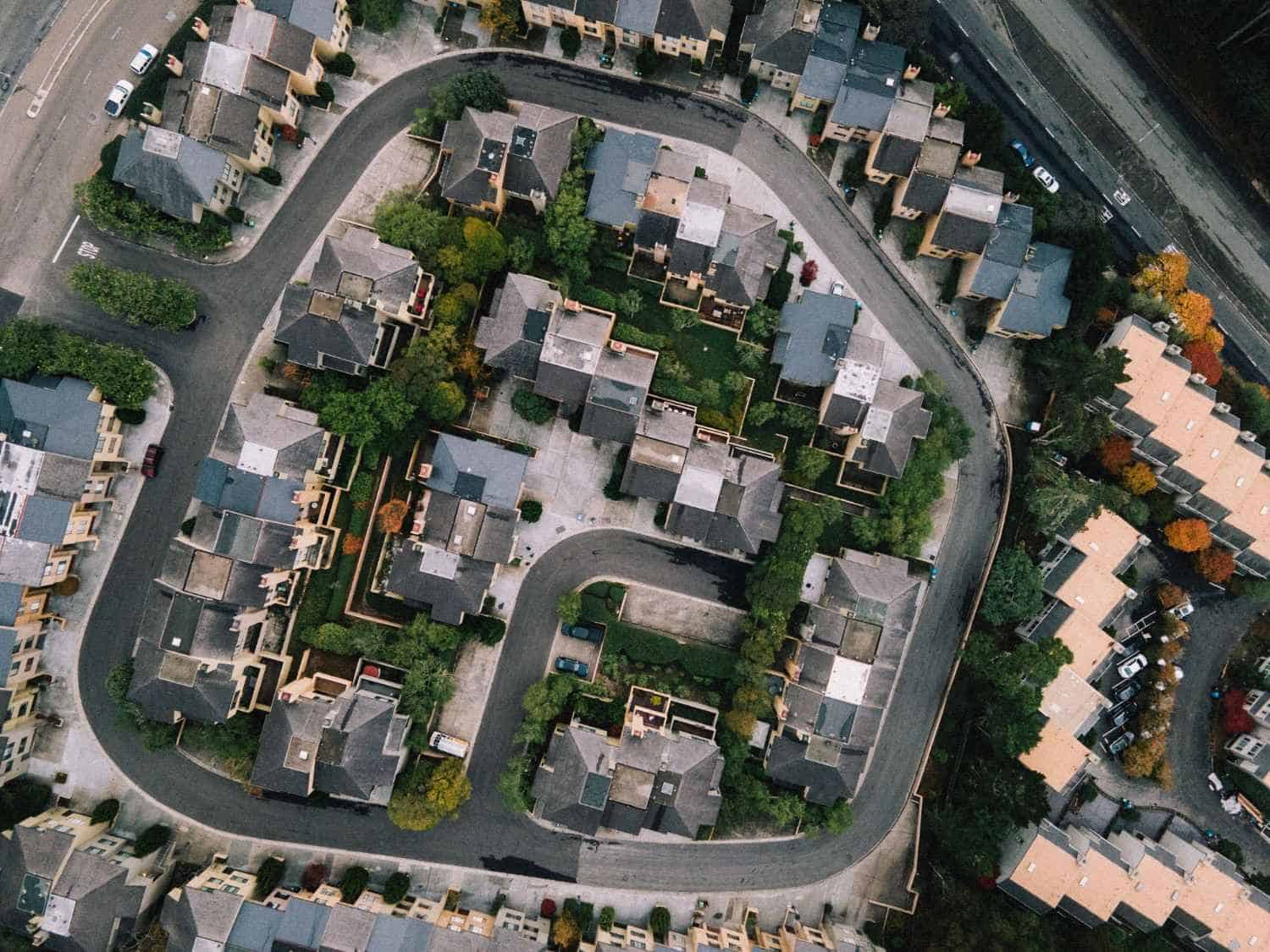 An aerial, birds-eye view of a densely arranged townhouse development and looping residential street in Olympia, Washington, showing meticulously planned landscaping and property layouts managed by professional HOA services.