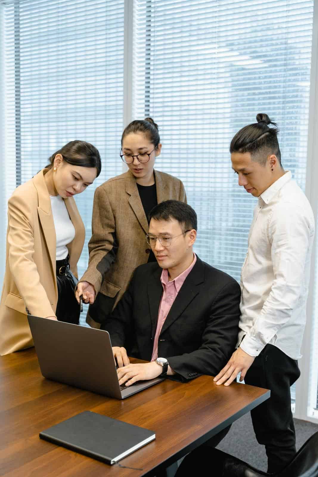 A professional HOA management team in Salem, Oregon, collaborating around a laptop computer in an office setting to review community guidelines, budgets, and property development plans.
